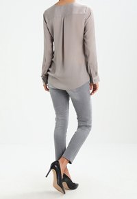 Blusa grigia chiaro a maniche lunghe con piega sulla schiena, abbinata a jeans grigi chiaro aderenti e scarpe con tacco alto nere.