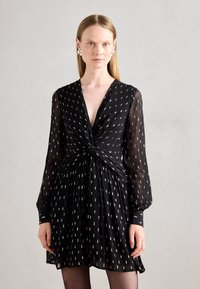 Abito nero realizzato in tessuto trasparente con maniche lunghe, scollo a V profondo, dettaglio intrecciato in vita e piccoli motivi bianchi su tutta la superficie.