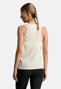 Top in beige chiaro con una texture liscia, design senza maniche e un sottile dettaglio del logo sul retro; abbinato a leggings neri.
