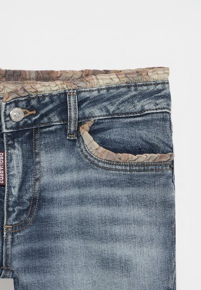 Jean en denim avec lavage délavé, bouton en métal et bordure en tissu fleuri sur la ceinture et les bords des poches, montrant la partie avant supérieure.