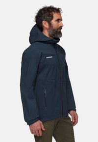 Veste imperméable navy avec capuche, zips et un design épuré. Comprend un logo sur la poitrine et des poches latérales.