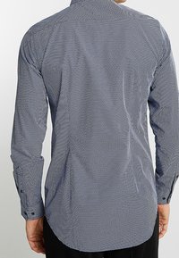 Uomo che indossa una camicia a maniche lunghe, abbottonata, a fantasia blu navy e bianca vista di spalle.
