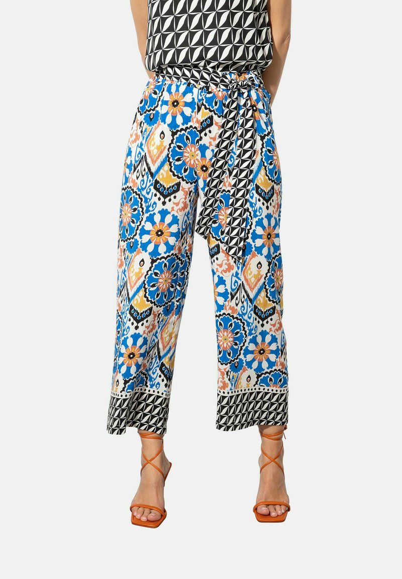 Bloemmotief brede broek in blauw, oranje en zwart, met een gestrikte taille en een geometrische accent aan de zoom. Gecombineerd met oranje strappy hakken.