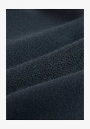 Tamsiai mėlynas audinys su minkšta, tekstūruota paviršiaus danga, kuriame matomos subtilios raukšlės ir nelygūs sulenkimai. Medžiaga atrodo stora ir šiek tiek pūkuota.