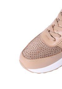 Scarpa sportiva beige con tomaia in suede perforato, lacci piatti, linguetta imbottita e suola in gomma bianca. Caratterizzata da un design minimalista e una texture liscia.