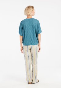 Ciklameno zigzaguotomis raštinėmis viršuje su trumpomis rankovėmis, derinamu su plačiomis juostuotomis kelnėmis kreminės, geltonos, mėlynos ir žalios spalvų atspalvių.