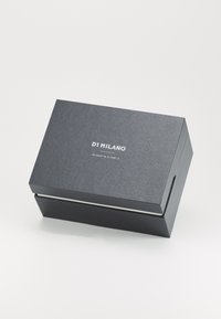 Caja de regalo texturizada en negro con tapa, que presenta texto impreso en blanco en la parte superior. El diseño incluye un acento plateado a lo largo del borde de apertura.