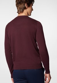 Bordowy sweter z długim rękawem, posiadający prążkowane mankiety i dół, charakteryzujący się gładką fakturą oraz okrągłym dekoltem. Widok z tyłu ukazuje detale szwów na ramionach.