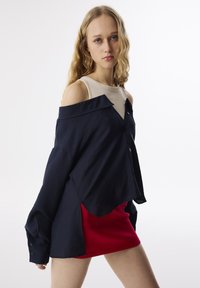 Marineblauw oversized blouse met textured stof en off-shoulder ontwerp. Gecombineerd met een rode mini rok met een gladde textuur.
