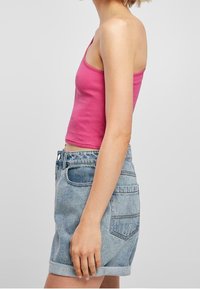 Top de tirantes de color rosa con canalé, combinado con pantalones cortos de mezclilla claros de cintura alta. Los pantalones cortos tienen puños enrollados, bolsillo frontal y detalles de bolsillo trasero con parche.