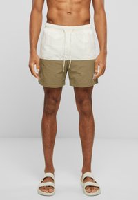 Short de bain pour homme avec une partie supérieure blanche et une partie inférieure vert olive, fabriqué en tissu léger avec une taille élastique et un cordon de serrage.