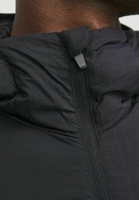 Black lightweight jacket with a hood, featuring a textured fabric, a front zipper, and a smooth finish around the neckline.