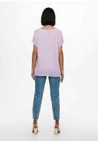 Top corto viola chiaro con un fit rilassato, abbinato a jeans blu alla caviglia con orli sfilacciati e sandali trasparenti con tacco alto.