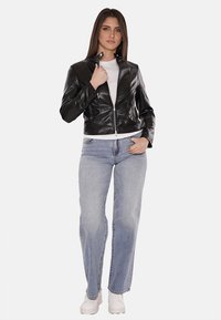 Giubbotto in pelle nera con design aderente, chiusura con zip e colletto rialzato, abbinato a jeans a gamba dritta blu chiaro e sneakers bianche.