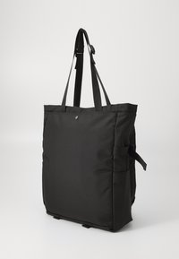 Czarna torba tote z regulowanymi paskami, o minimalistycznym wzornictwie i bocznymi kieszeniami, wyeksponowana na jednolitym białym tle.