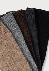 Cinq paires de chaussettes côtelées tricotées en beige, gris, marron, gris foncé et noir, présentant différentes nuances et textures.