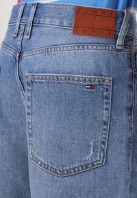Lyseblå denimjeans med en brun skinnmerkelapp merket "TOMMY JEANS" på livet og en liten trikolorlogo på baklommen.