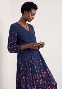 Marineblaues Kleid mit rosa floralem Stickmuster, das lange Puffärmel und ein V-Ausschnitt-Design aufweist. Glatter Stoff mit fließender Silhouette.