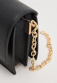 Borsa a mano in pelle nera testurizzata con forma curva, tracolla a catena dorata e dettagli in metallo per la chiusura.