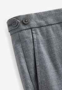 Pantalon en tissu gris avec une texture lisse, deux plis devant et deux boutons noirs à la taille.