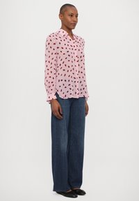 Light pink long-sleeve button-up shirt with red leaf patterns, paired with wide-leg dark blue denim jeans and black flat shoes.