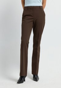 Pantalons taillés marron avec une texture lisse, design à jambe droite, poches avant et passants de ceinture, associés à des escarpins noirs à bout pointu.
