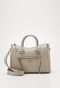 Jasnobeżowa skórzana torebka z dwoma uchwytami, regulowanym paskiem na ramię, przednią kieszenią na zamek i złotym zawieszonym logo "MK" na jednolitym tle.