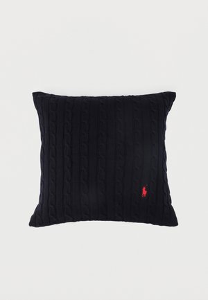 Coussin carré en tricot noir avec un petit logo brodé d'un joueur de polo rouge dans le coin inférieur droit sur fond blanc.