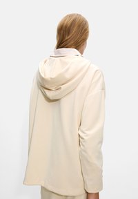 Light beige hoodie with a soft texture. Features a hood and a relaxed fit, with a slightly longer back hem and minimal stitching details.