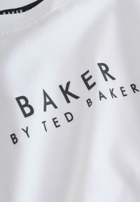 Balta medžiaga su juodu tekstu „BAKER BY TED BAKER“ parašytu storomis didžiosiomis raidėmis.