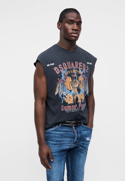 Jeune homme portant un débardeur noir à motifs avec les textes « DSQUARED2 » et « La vie est meilleure à la gym », associé à un jean bleu et une ceinture cloutée.