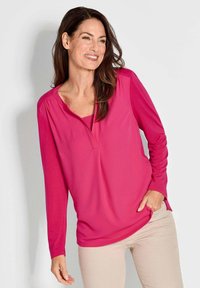 Maglietta a maniche lunghe di un vivace colore rosa con scollatura a V e spacchi laterali, realizzata in tessuto leggero, caratterizzata da una vestibilità comoda e una texture morbida.