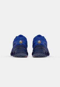 Een paar blauwe sport sneakers gezien van de achterkant, met "Air Max" merknaam en gestructureerde, donkere zolen op een witte achtergrond.