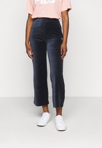 Mörkblå sammetsbyxor med hög midja och en liten logodetalj. Kombination med vita sneakers och en ljusrosa oversize t-shirt.