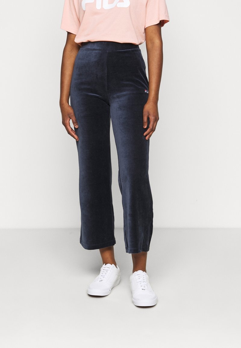 Mörkblå sammetsbyxor med hög midja och en liten logodetalj. Kombination med vita sneakers och en ljusrosa oversize t-shirt.