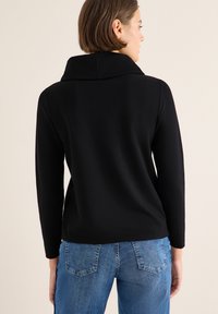 Zwarte top met lange mouwen en hoge kraag, gladde textuur, aansluitende silhouet, gecombineerd met lichtblauwe denim jeans met klassieke achterzakken.