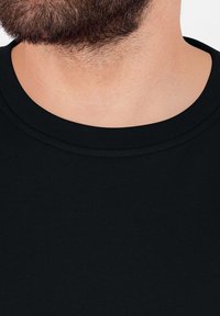 T-shirt en coton noir à col rond avec une encolure côtelée. Vue rapprochée de la texture du tissu et de la zone du cou, affichant une apparence lisse et unie.