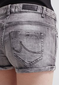 Pantalones cortos de mezclilla gris con dobladillo deshilachado, que presentan un diseño de bolsillos cosidos y una etiqueta de marca de cuero en la cintura.