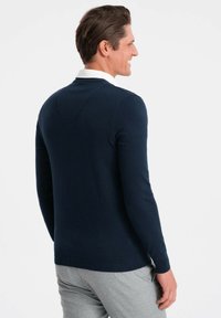 Maglione leggero blu navy con maniche lunghe e orlo a costine, caratterizzato da un sottile dettaglio a forma di V sulla schiena.