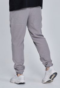 Szürke fleece jogger nadrág elasztikus mandzsettákkal és oldalsó zsebekkel, világos sportcipőkkel, melyek hálós részletekkel és texturált talppal rendelkeznek.