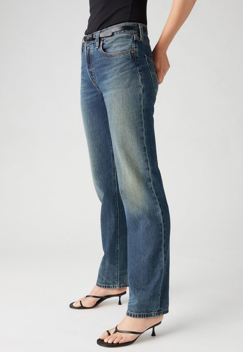Jeans din denim albastru cu un finisaj uzat, croială dreaptă, design cu cinci buzunare și o curea neagră. Combinat cu sandale negre cu toc.
