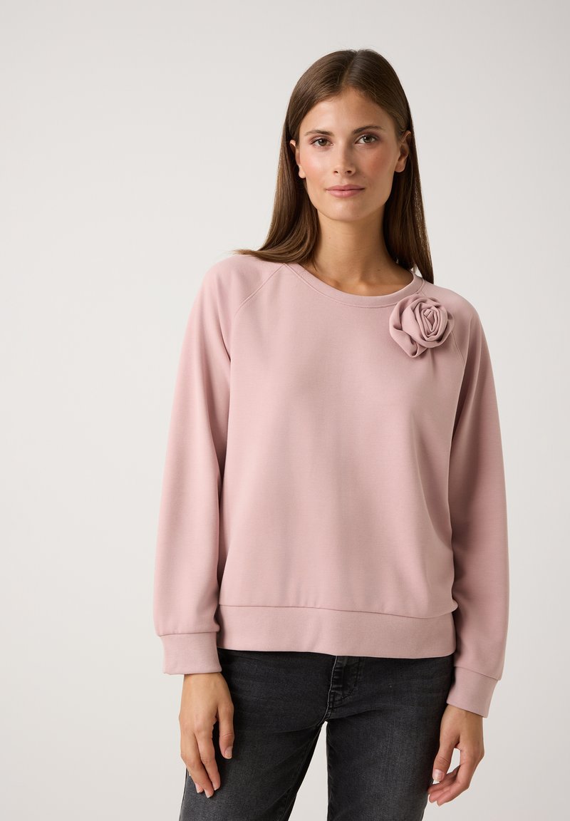 Sweat-shirt rose clair en tissu doux, avec un col rond et des poignets côtelés. Accent de rose en tissu décoratif sur l'épaule gauche.