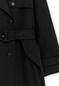 Trench-coat noir avec ceinture boutonnée, poches à rabat et poignets à boutons, présenté sur un fond blanc.