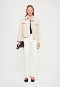 Giacca cropped beige con due tasche frontali, abbinata a pantaloni bianchi a gamba larga e décolleté nere a punta. Borsa nera piccola in mano.