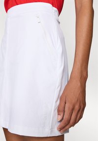 White skirt featuring a sleek design, zippered side pockets, and a subtle Calvin Klein logo embossed at the hem. Made from smooth fabric.