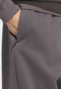 Graue Sweatshirtmaterial mit einer Tasche auf Taillenhöhe, feiner Textur und doppellagigem Bündchen-Design. Minimalistisch und funktional.