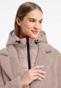 Lichtbeige buitenkleding met een gestructureerde fleece buitenkant en een gladde, geïsoleerde binnenlaag met een capuchon. Ritsluiting en verstelbare toggles.