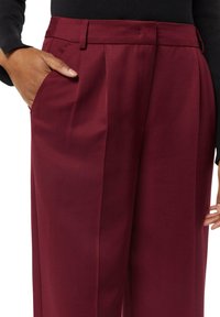 Burgundowe dopasowane spodnie z wyprasowanym przodem, kieszeniami bocznymi i gładką teksturą. Posiadają paski w pasie oraz luźny krój.