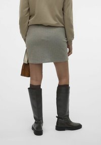 Šedá sukni ve vzoru herringbone, těsně přiléhající design, délka nad kolena. V kombinaci s vysokými černými koženými botami a hnědými pletenými ponožkami. Jednoduchá hnědá taška.