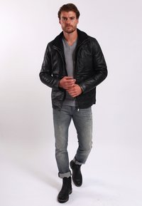 Svart läderjacka med hög krage, dragkedjestängning, strukturerad yta, kombinerad med en grå V-ringad tröja och ljusblå jeans, ankelstövlar.